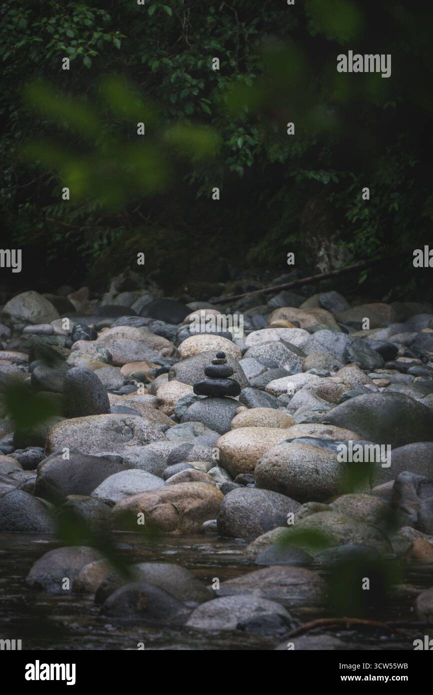 Le pietre lisce sono impilate con cura vicino a un fiume tranquillo. La lussureggiante vegetazione circonda l'area, creando un tranquillo ambiente naturale per riflettere Foto Stock
