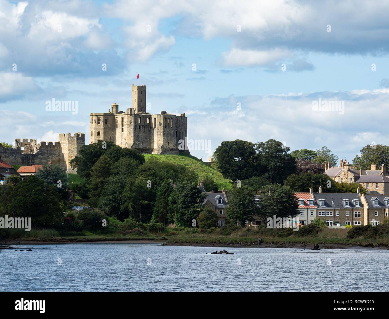 Il castello di Warkworth si affaccia sulle case lungo il fiume a Amble in una giornata di sole Foto Stock
