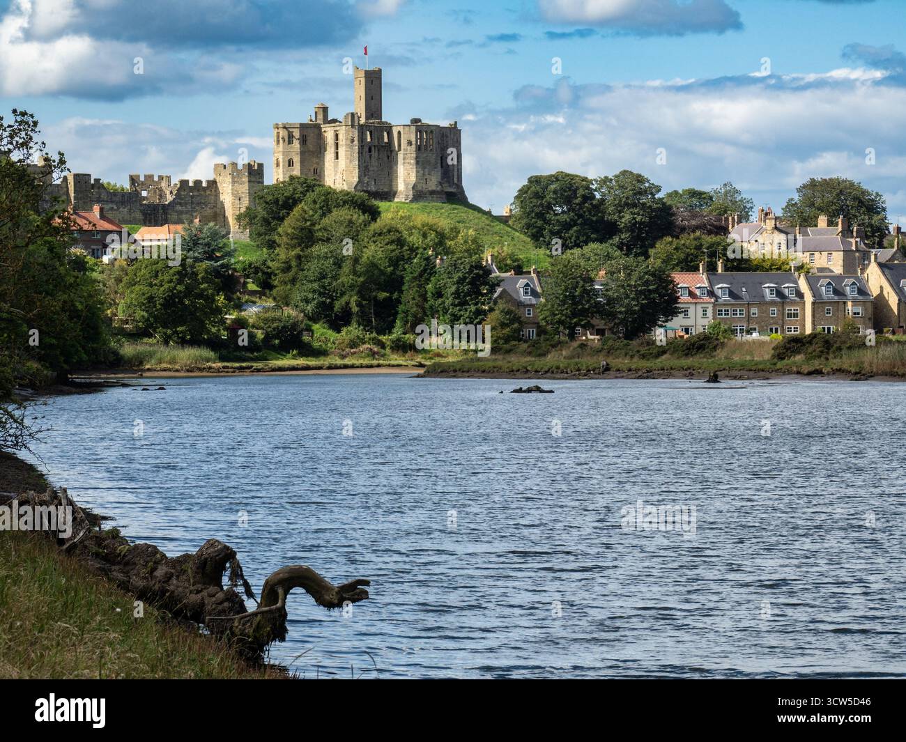Il castello di Warkworth si affaccia sulle case lungo il fiume a Amble in una giornata di sole Foto Stock
