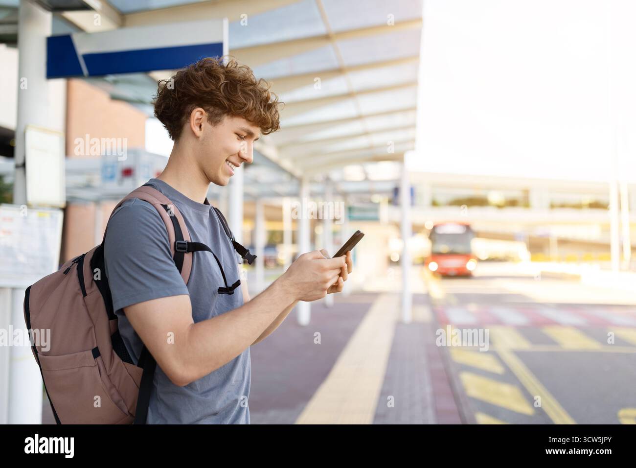 Vista laterale del viaggiatore sorridente che utilizza lo smartphone sulla piattaforma dell'aeroporto Foto Stock
