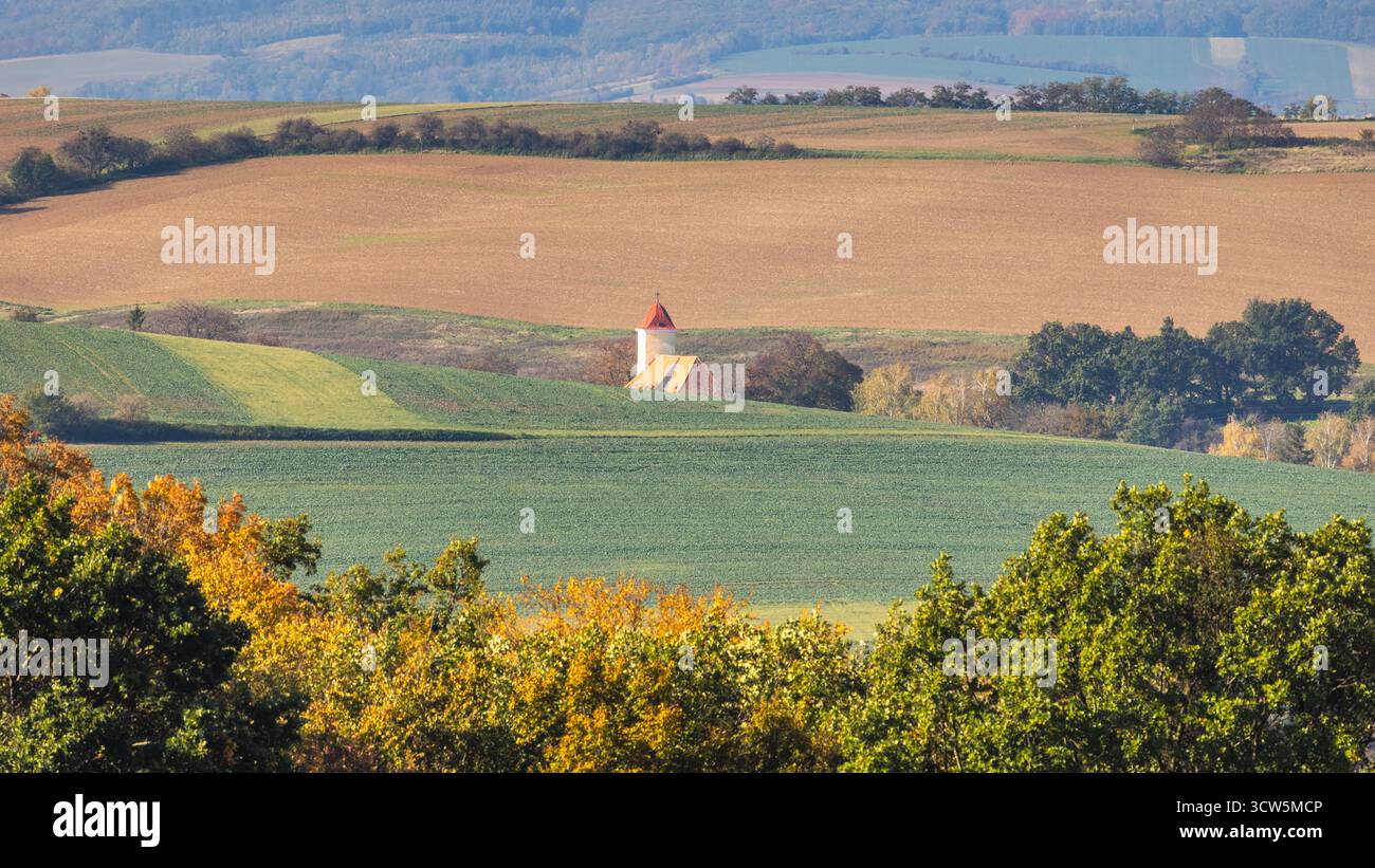 Paesaggio rurale caratterizzato da colline ondulate, campi coltivati e un affascinante edificio con un tetto rosso sotto la luce del giorno. Regione Moravia della Repubblica Ceca Foto Stock