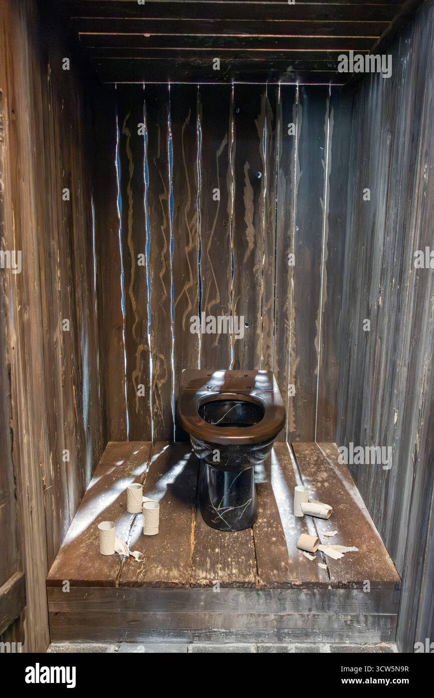 Gabinetto aperto in legno con pareti a tavolino e residui di carta igienica sul pavimento Foto Stock