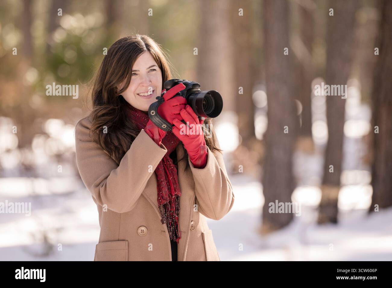 Una donna sorridente con guanti rossi tiene la macchina fotografica nella foresta innevata di Tahoe Foto Stock