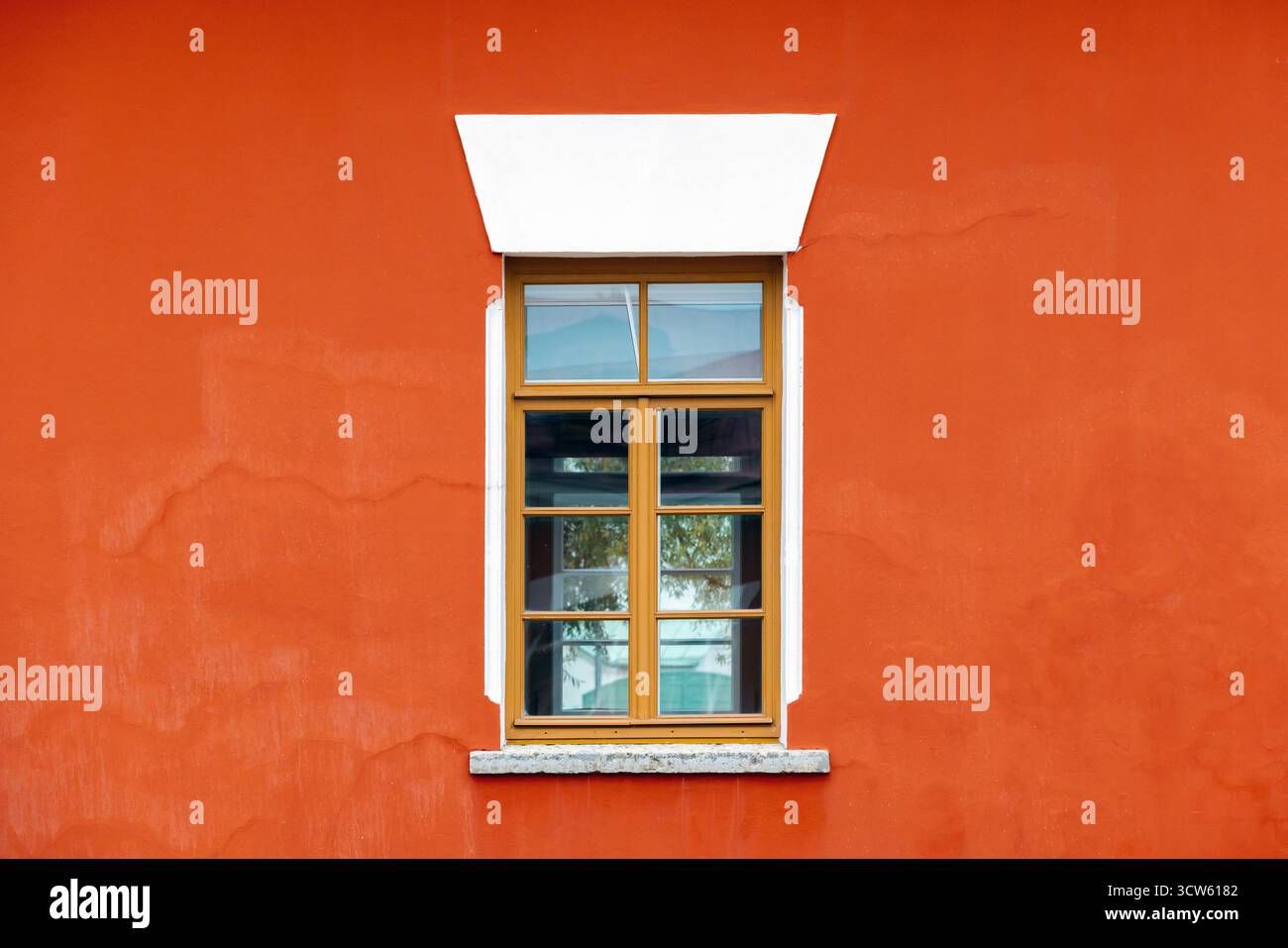 L'audace parete arancione incornicia una classica finestra in legno con pannelli di vetro. Le finiture bianche e la soglia in pietra mettono in risalto i dettagli architettonici, creando un ambiente caldo e invitante Foto Stock