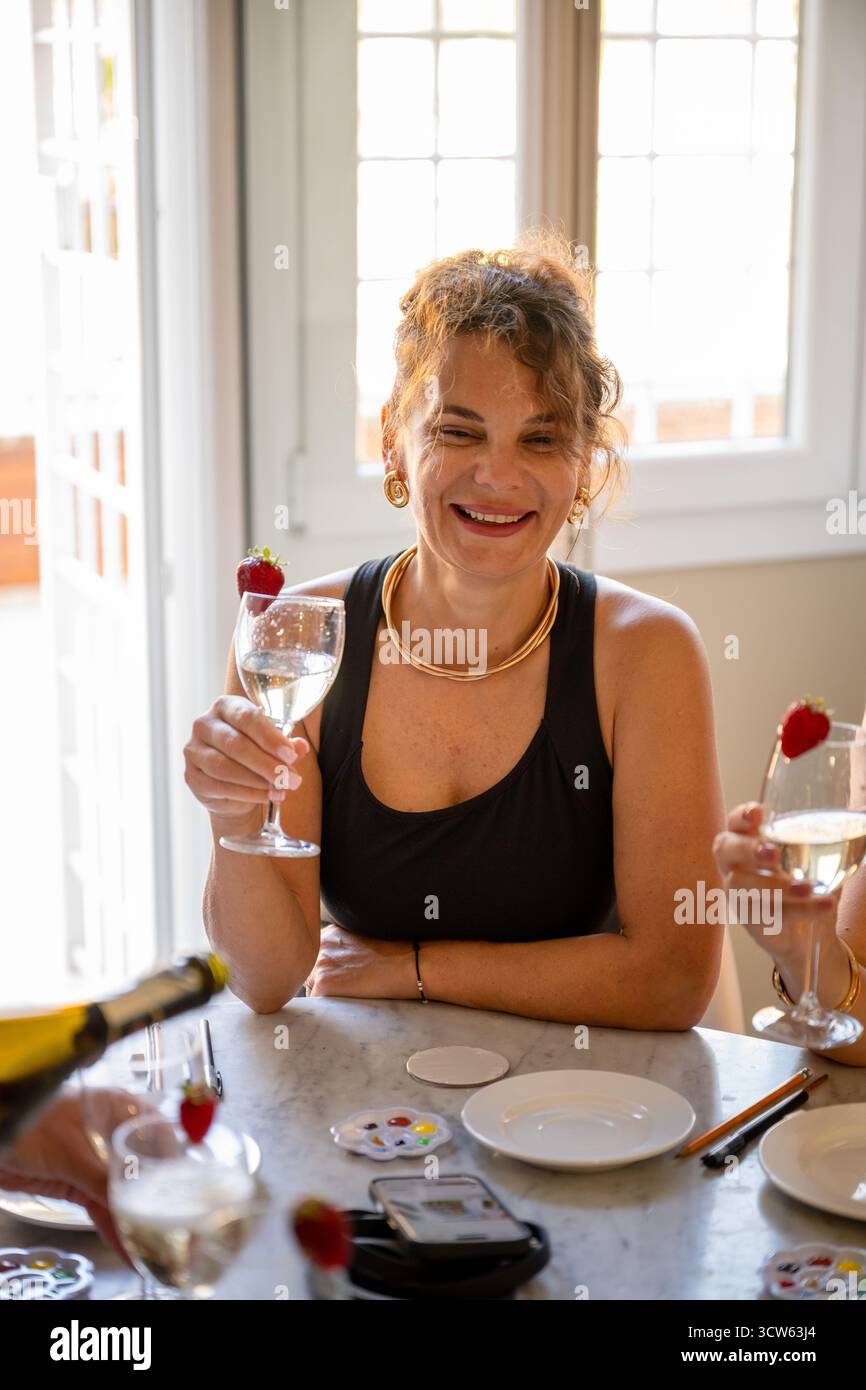 Donna in abito nero che sorride e tiene un bicchiere di vino all'interno Foto Stock