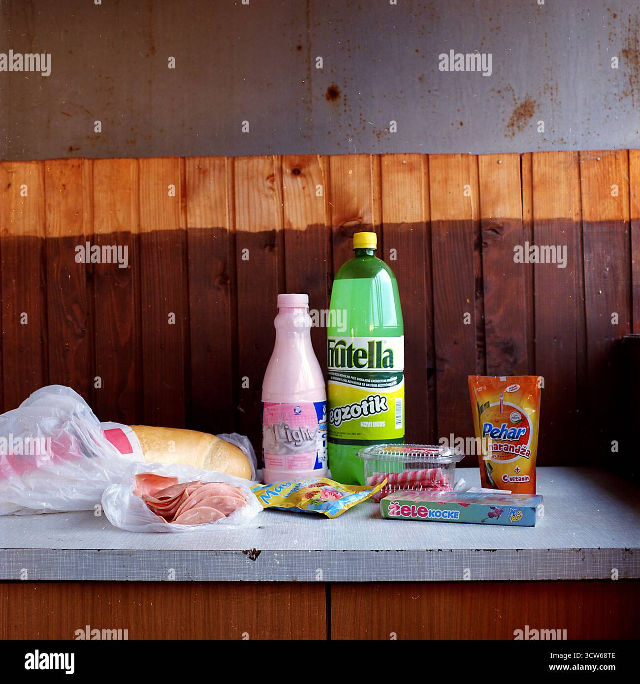 Immondizia con salame, pane, mayo, yogurt, soda esotica a buon mercato, caramelle e una tazza rotta sistemata su uno scaffale prima di placcare. Luce naturale. Foto Stock