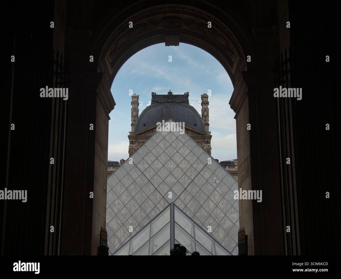La Piramide del Louvre incorniciata dall'Archway al tramonto, l'iconica piramide di vetro e la storica cupola del palazzo, incorniciata da un arco di pietra scura sotto a. Foto Stock