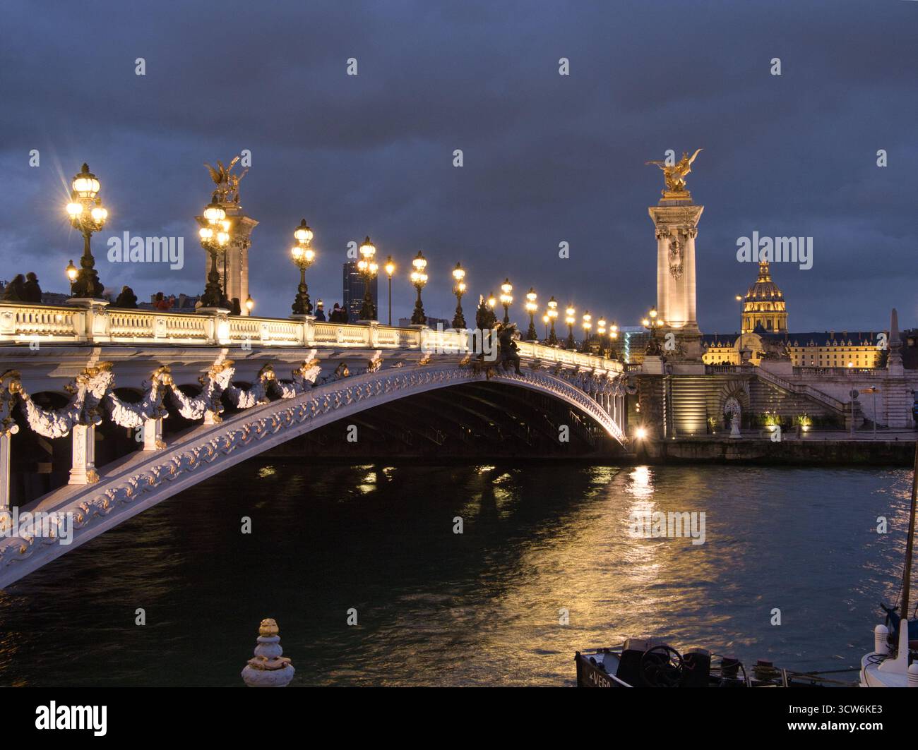 Ponte Alexandre III illuminato di notte - il maestoso ponte Pont Alexandre III illuminato in modo luminoso contro un cielo buio e nuvoloso con san dorato Foto Stock