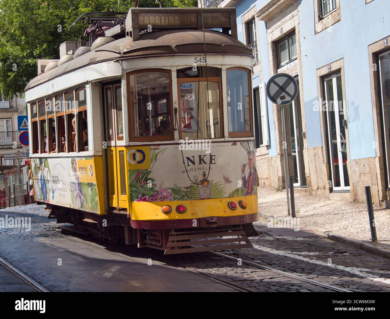 Tram d'epoca pubblicizzato per l'arrampicata sulla collina acciottolata di Lisbona - Un tram bianco e giallo d'epoca con pubblicità laterali colorate per un marchio di bevande Foto Stock