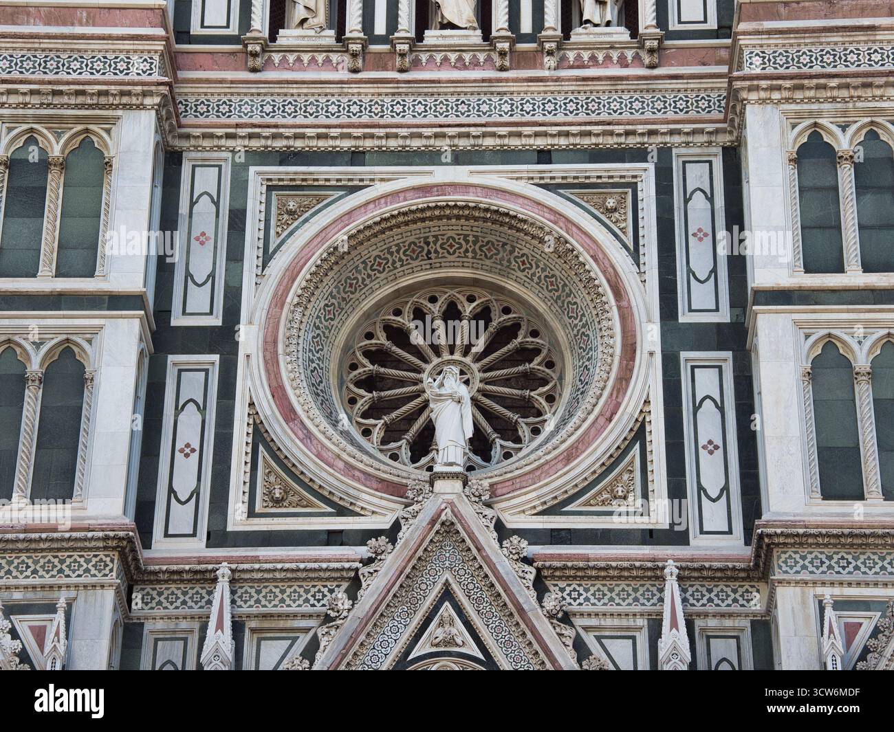 Dettaglio del rosone del Duomo e della statua della Vergine Maria - dettaglio centrale della facciata in marmo ornata del Duomo di Firenze, incentrato sul rosone gotico Foto Stock