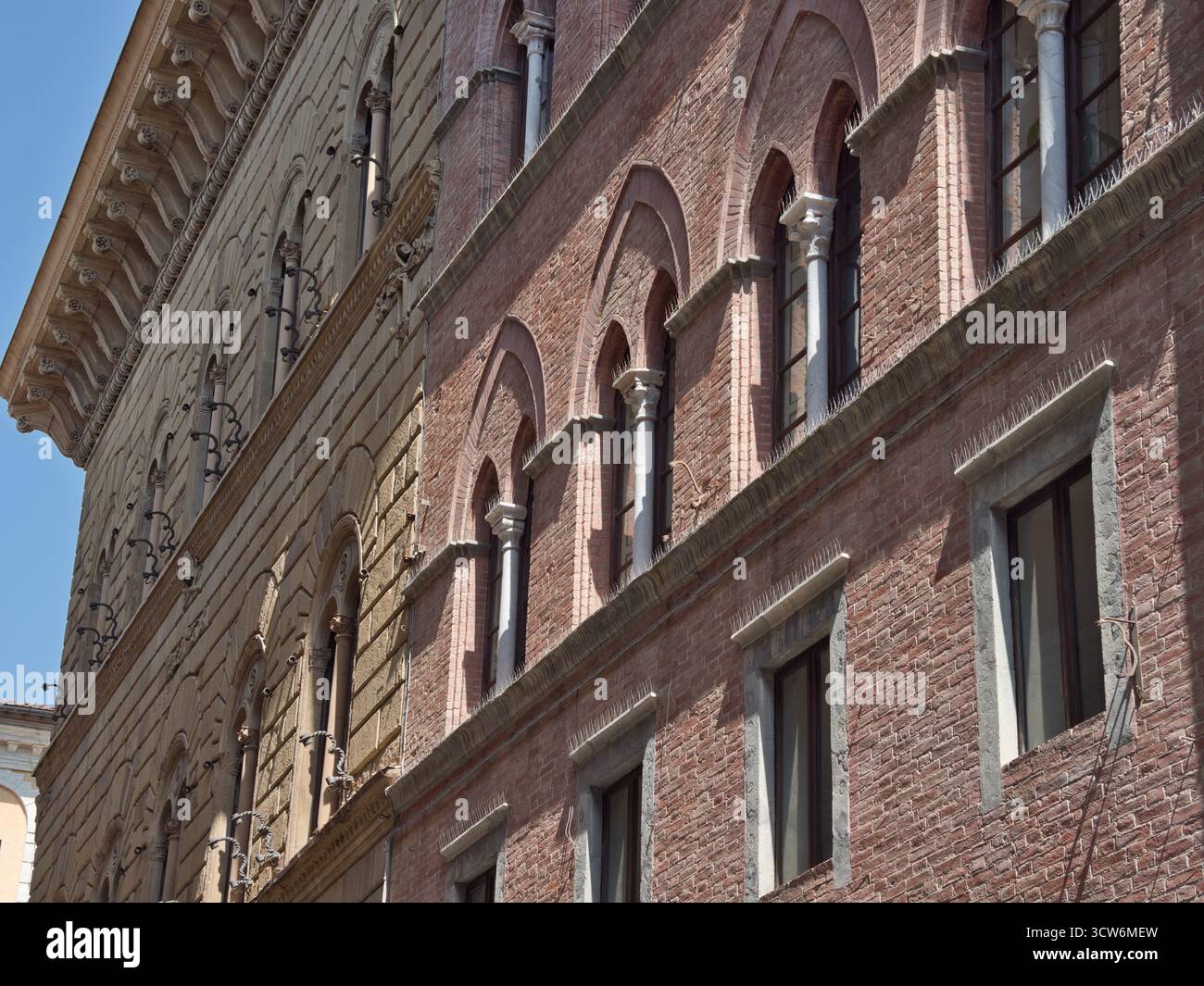 Facciata in mattoni toscani con finestre ad arco e colonne - Vista diagonale che mostra la consistenza della facciata in mattoni rossi di un edificio storico e dell'arco multiplo Foto Stock