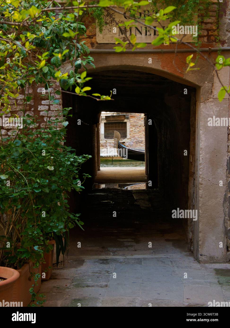 Vista ad arco della Gondola nascosta sul piccolo canale veneziano - Un sottoportego scuro ad arco (sottopassaggio) incornicia uno scorcio di prua di una gondola su un piccolo nascondiglio Foto Stock