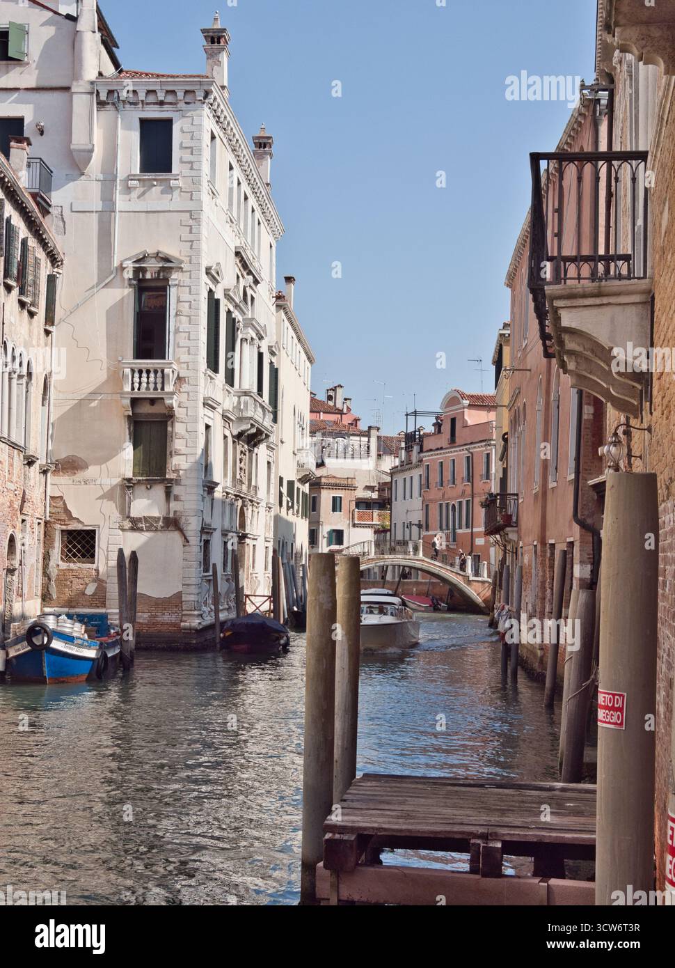 Luminoso Canale Veneziano con Palazzo bianco e Ponte - Un canale veneziano illuminato dal sole incorniciato da edifici storici, con un prominente palazzo bianco, un passaggio Foto Stock