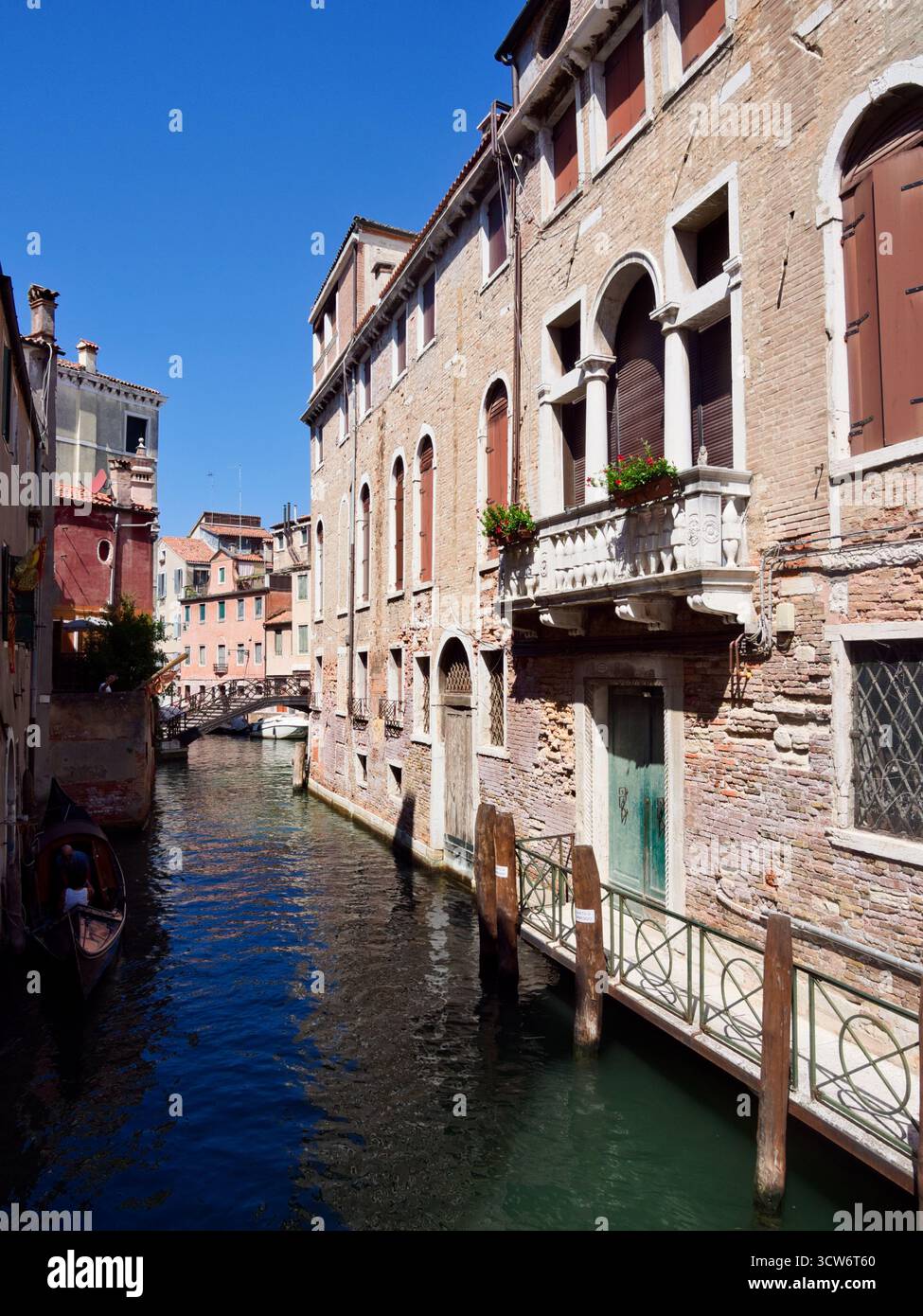 Classico canale veneziano in mattoni con balconi e Ponte - Uno stretto e storico canale veneziano fiancheggiato da edifici in mattoni rossi con vento gotico ad arco Foto Stock