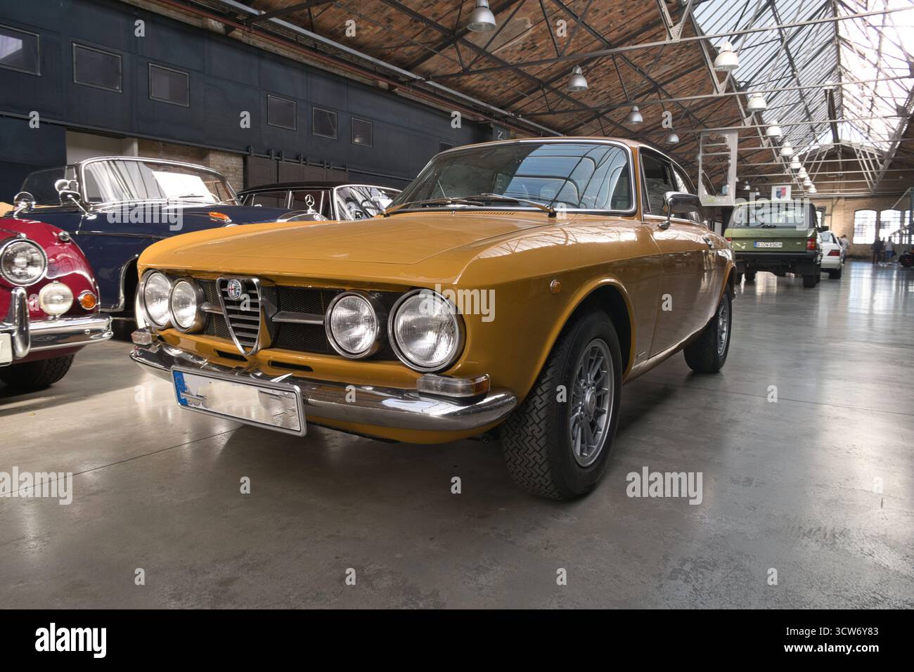 Vintage Yellow Italian Coupé nello showroom - Vista frontale di una classica coupé sportiva italiana gialla con finiture cromate, parcheggiata in una spaziosa e luminosa Foto Stock