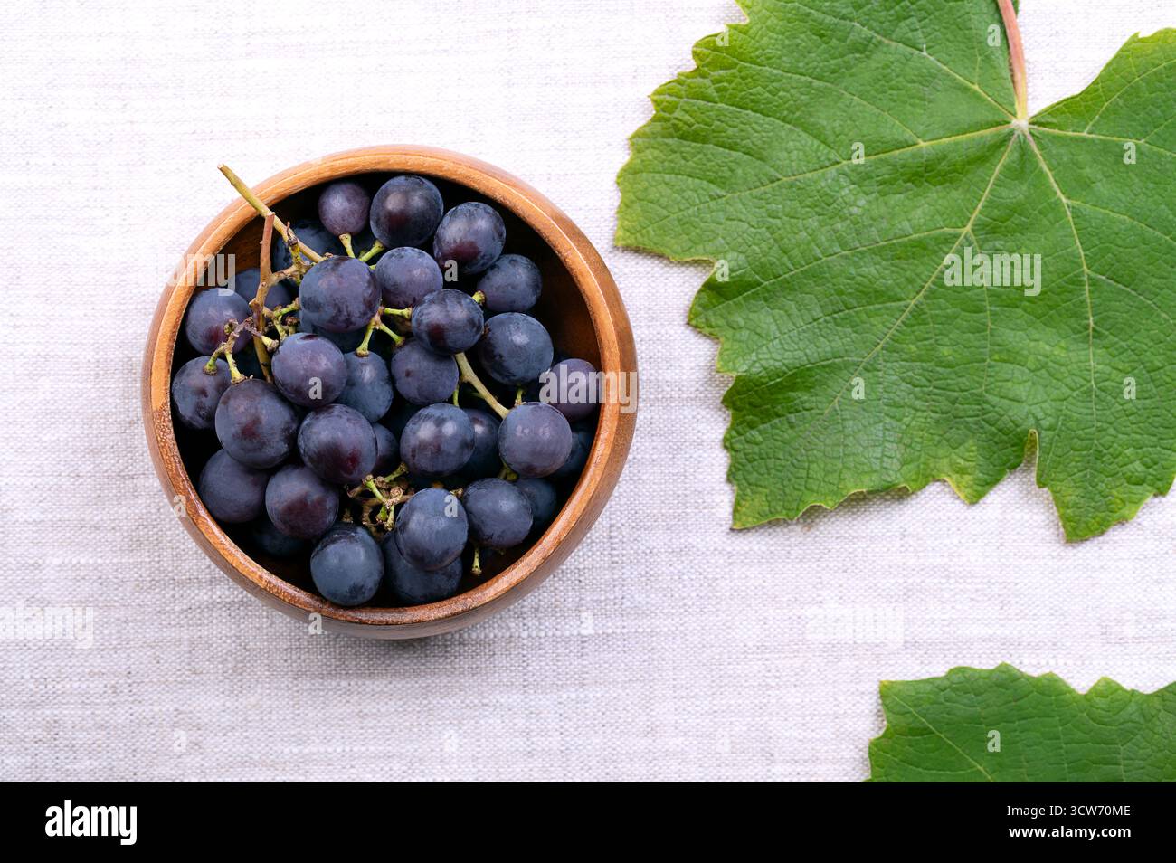 Uva blu del comune vitigno, in una ciotola di legno, su lino, dall'alto. Frutti maturi appena raccolti di Vitis vinifera, una specie europea. Foto Stock