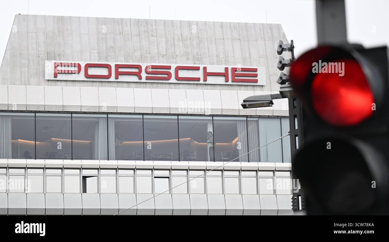 Stoccarda, Germania. 10 ottobre 2025. Un semaforo rosso brilla di fronte a un edificio con il logo Porsche presso la sede centrale del produttore di auto sportive a Stoccarda-Zuffenhausen. Porsche AG fa parte del gruppo Volkswagen ed è nota per i suoi veicoli sportivi e di lusso. Crediti: Bernd Weißbrod/dpa/Alamy Live News Foto Stock