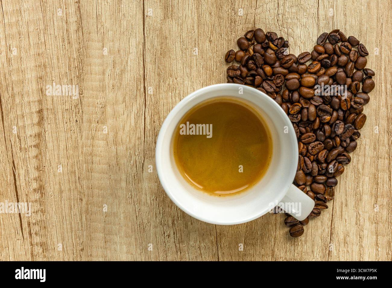 Vista dall'alto di una tazza di caffè con chicchi di caffè a forma di cuore su un tavolo di legno. Simbolo dell'amore per il caffè, la colazione e le accoglienti vibrazioni mattutine. Foto Stock