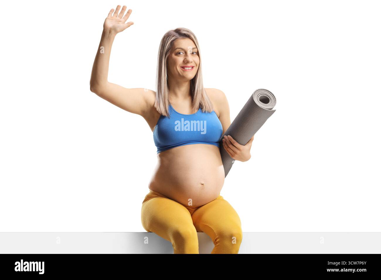 Donna incinta con un tappetino da ginnastica seduto su un pannello vuoto e che ondeggia isolata su sfondo bianco Foto Stock