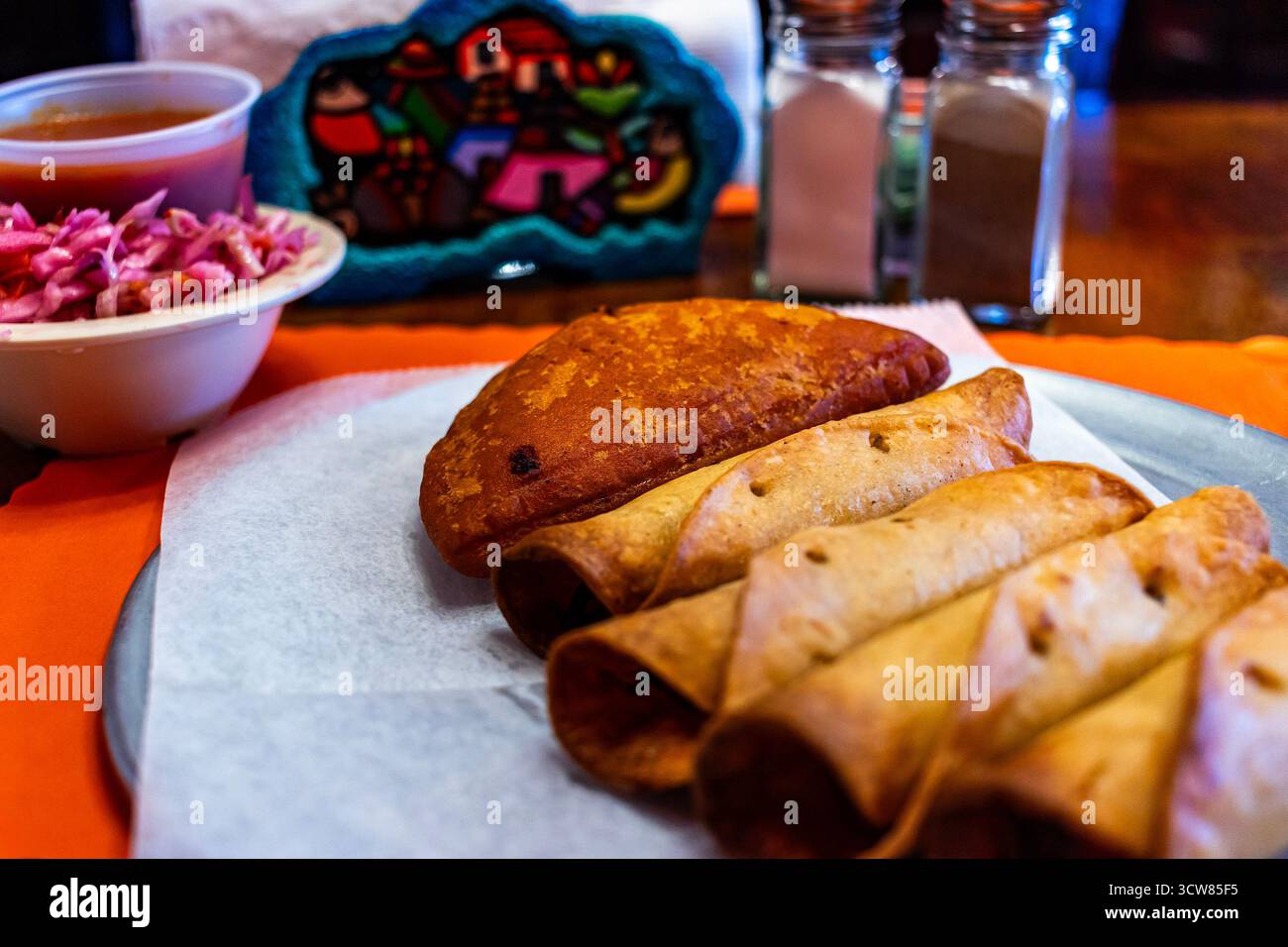 Tradizionale pasto salvadoregno con taquito fritto dorato e un'empanada croccante, servito con curtido (sciamano di cavolo sottaceto) e salsa di pomodoro Foto Stock