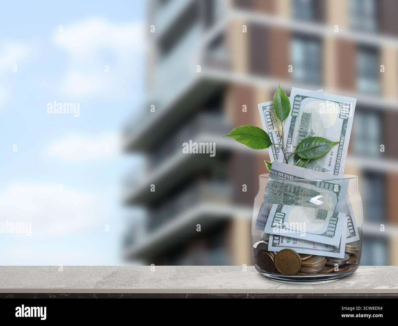 Barattolo con dollari e monete contro il condominio. Risparmiare denaro per comprare un appartamento Foto Stock