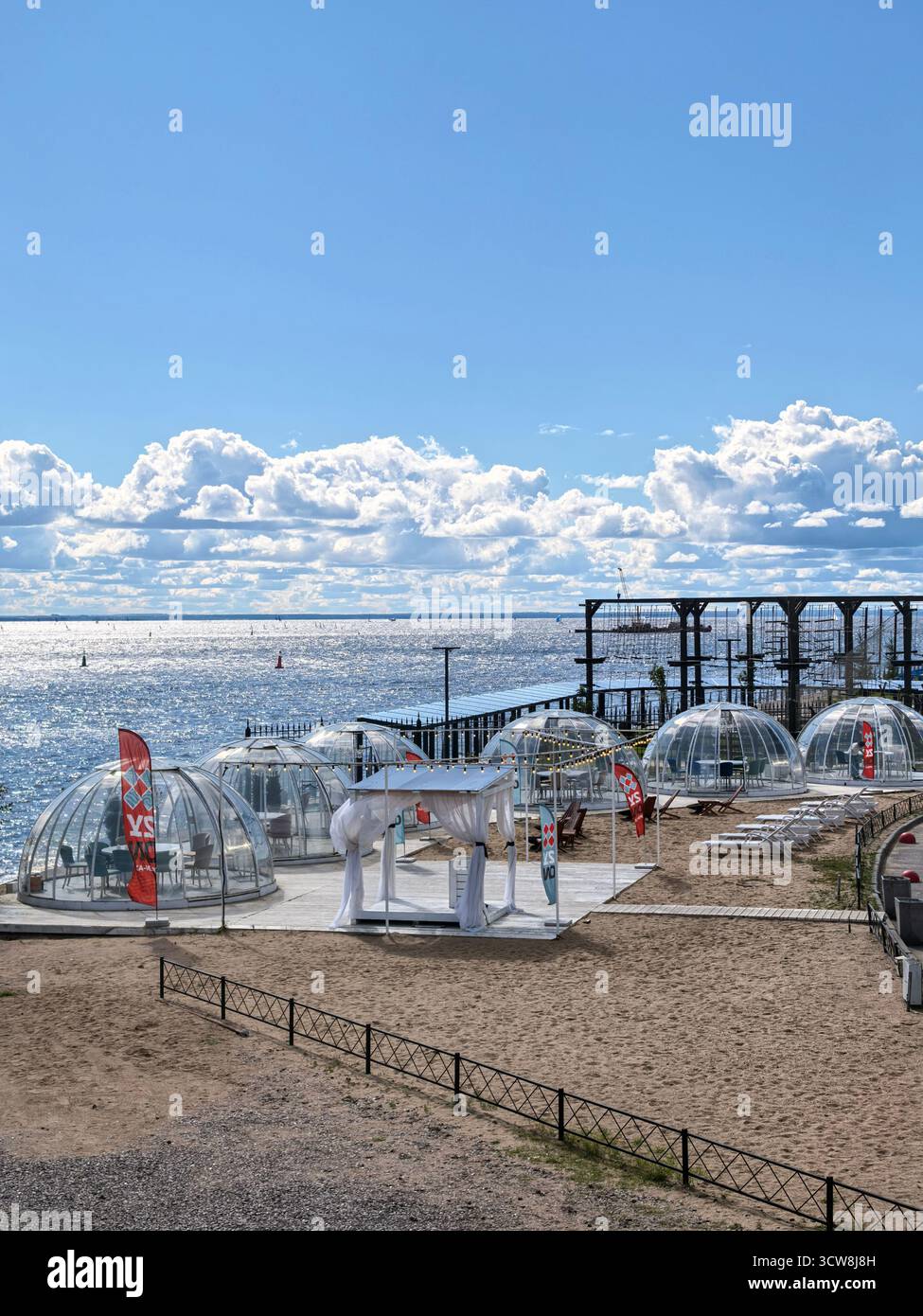 San Pietroburgo, Russia - 08.20.2025. Le esclusive cupole di vetro che proteggono il vento su una spiaggia sabbiosa servono da caffetterie presso il Golfo di Finlandia. Foto Stock