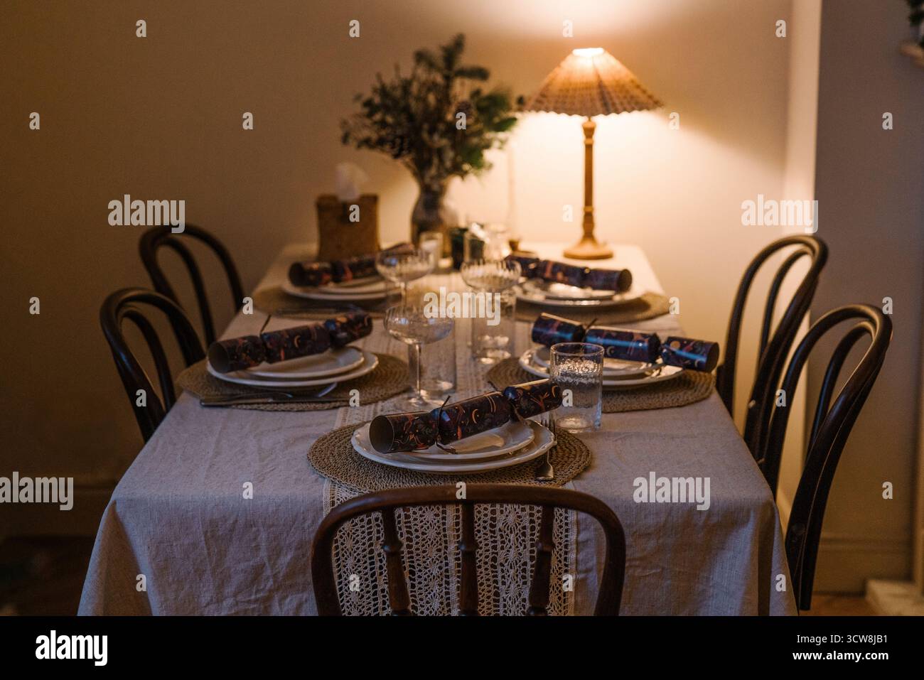 Tavolo da pranzo con luce calda e arredi rustici, cracker natalizi, candele e un'accogliente atmosfera invernale. Foto Stock