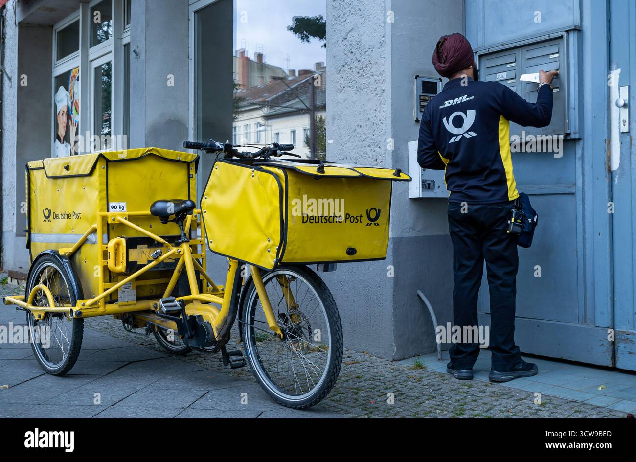 Operaio di Deutsche Post che consegna la posta a Berlino, Germania. La scena di strada di tutti i giorni riflette la diversità urbana e la vita quotidiana in una moderna città europea. Foto Stock