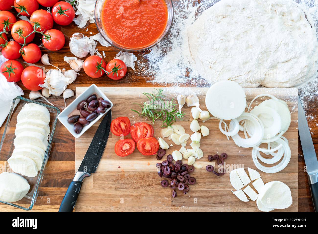 Vista dall'alto dei classici ingredienti della pizza italiana: Mozzarella, farina, aglio, salsa di pomodoro, olive, e cipolle, predisposte per la preparazione della cottura in casa. Foto Stock