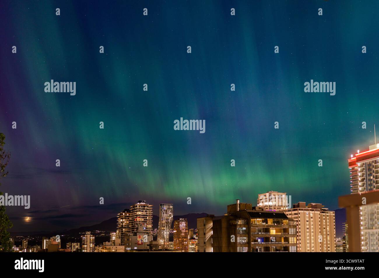 Le colorate luci boreali illuminano il cielo notturno sopra la città. Gli edifici riflettono la straordinaria esposizione, creando una scena urbana mozzafiato Foto Stock