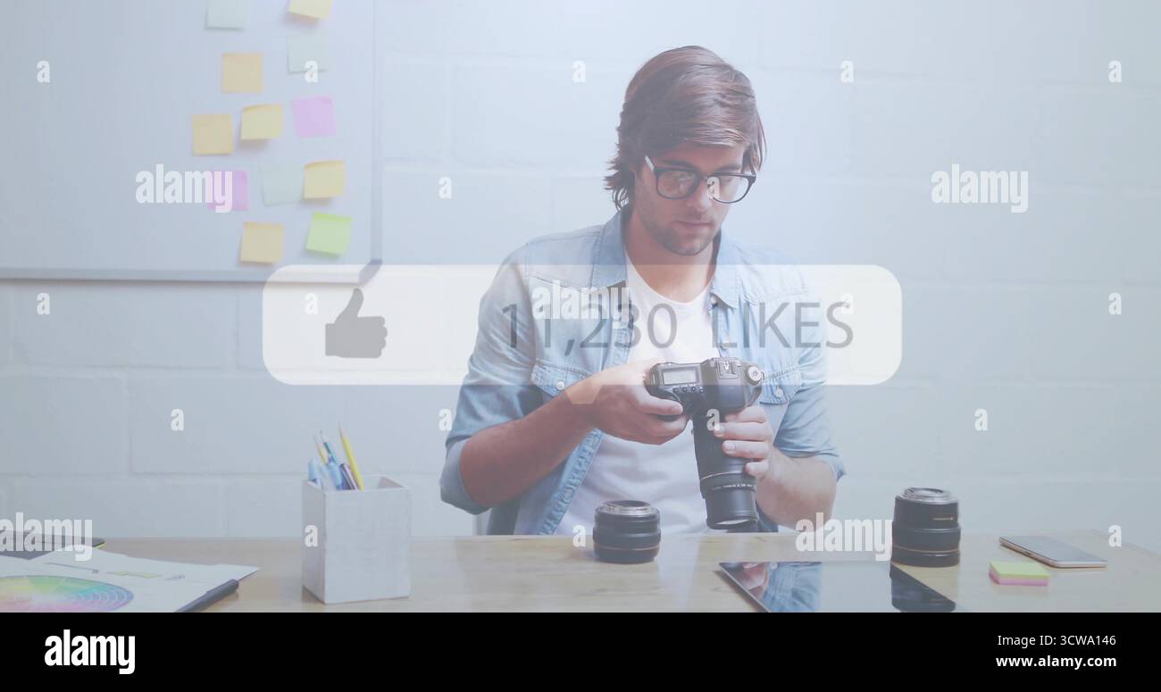 Fotografo che ispeziona il corpo della fotocamera DSLR presso una scrivania in legno nell'ufficio creativo, con obiettivi e tablet Foto Stock
