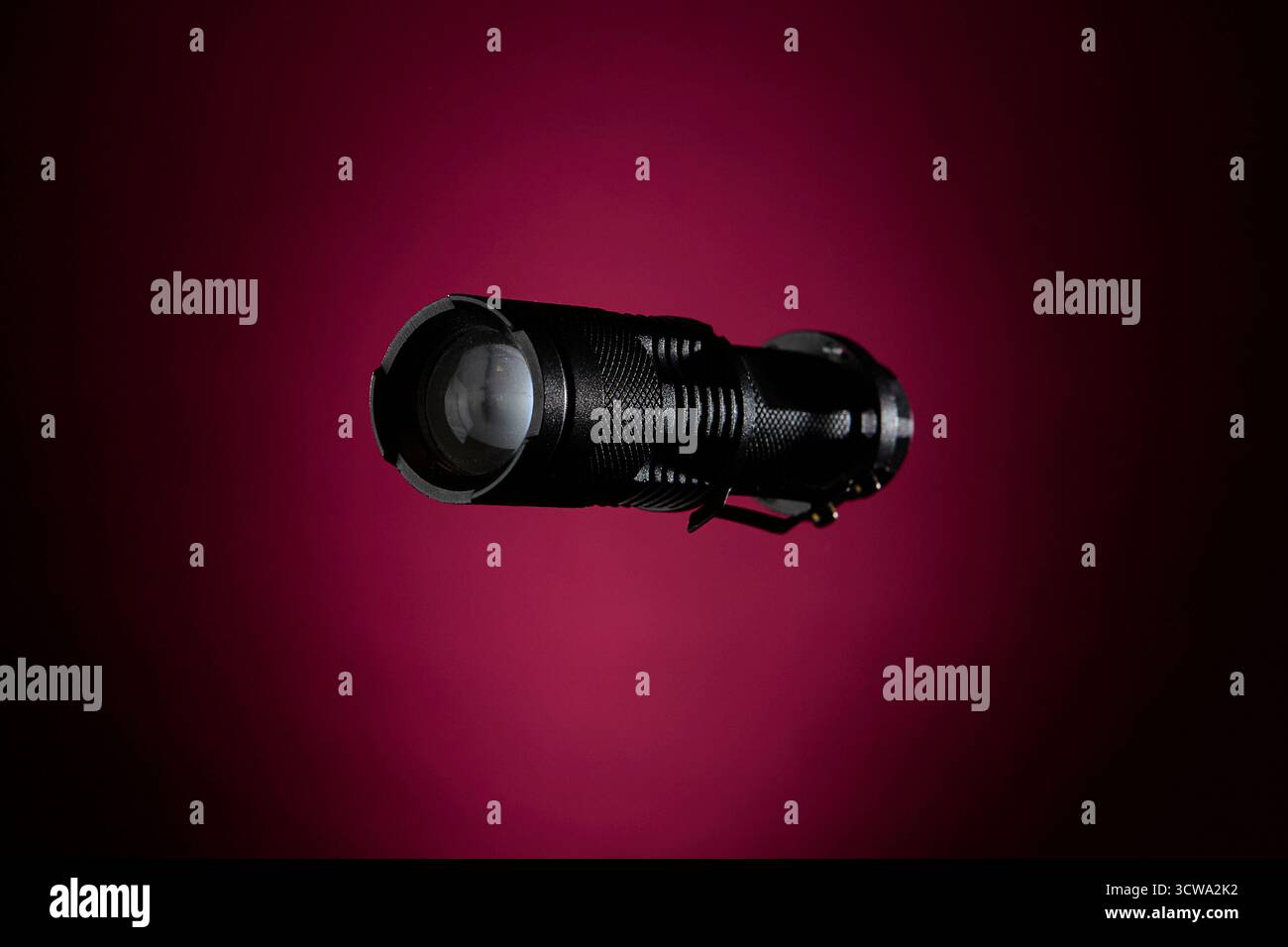 Torcia nera compatta catturata su sfondo magenta con illuminazione controllata. Simbolo di preparazione, visione notturna e tecnologia portatile per tr Foto Stock