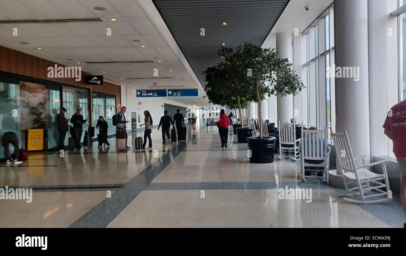 Charlotte, North Carolina, USA, 10 ottobre 2025: Le persone con bagagli attraversano un atrio luminoso e spazioso all'Aeroporto Internazionale Douglas di Charlotte. Foto Stock