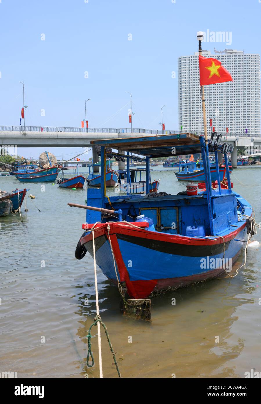 NHA TRANG, VIETNAM - 25 APRILE 2025. Barche da pesca sul fiume Cai, il ponte, grattacieli e bandiere nazionali Foto Stock
