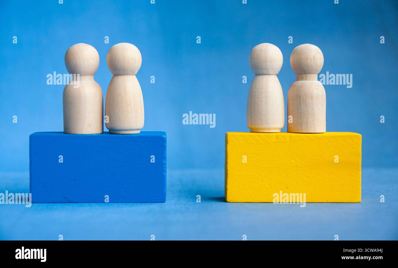 Figure in legno raggruppate su blocchi blu e gialli simboleggiano la divisione sociale, la gerarchia della leadership e le opportunità Foto Stock