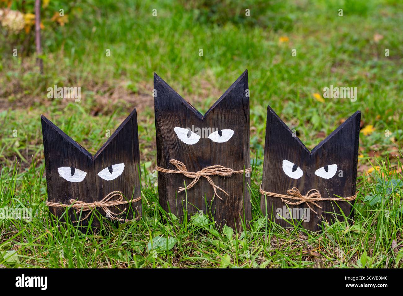 Tre gatti in legno fatti in casa su erba verde nel giardino autunnale per la decorazione, primo piano. Gatti decorativi in legno su sfondo naturale Foto Stock