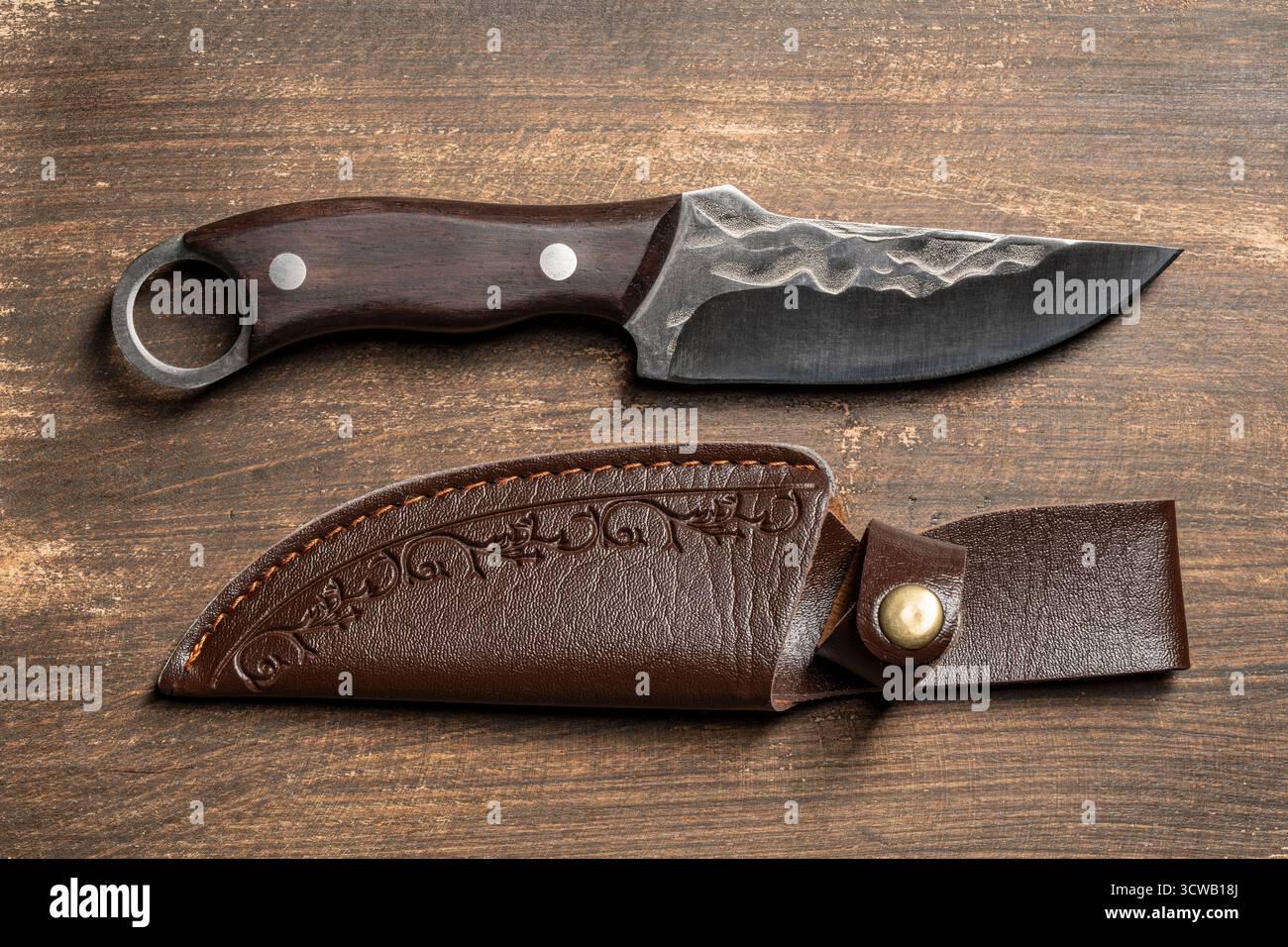 Coltello forgiato affilato realizzato a mano con manico in legno. Coltello da caccia in acciaio con custodia in pelle, primo piano, vista dall'alto Foto Stock