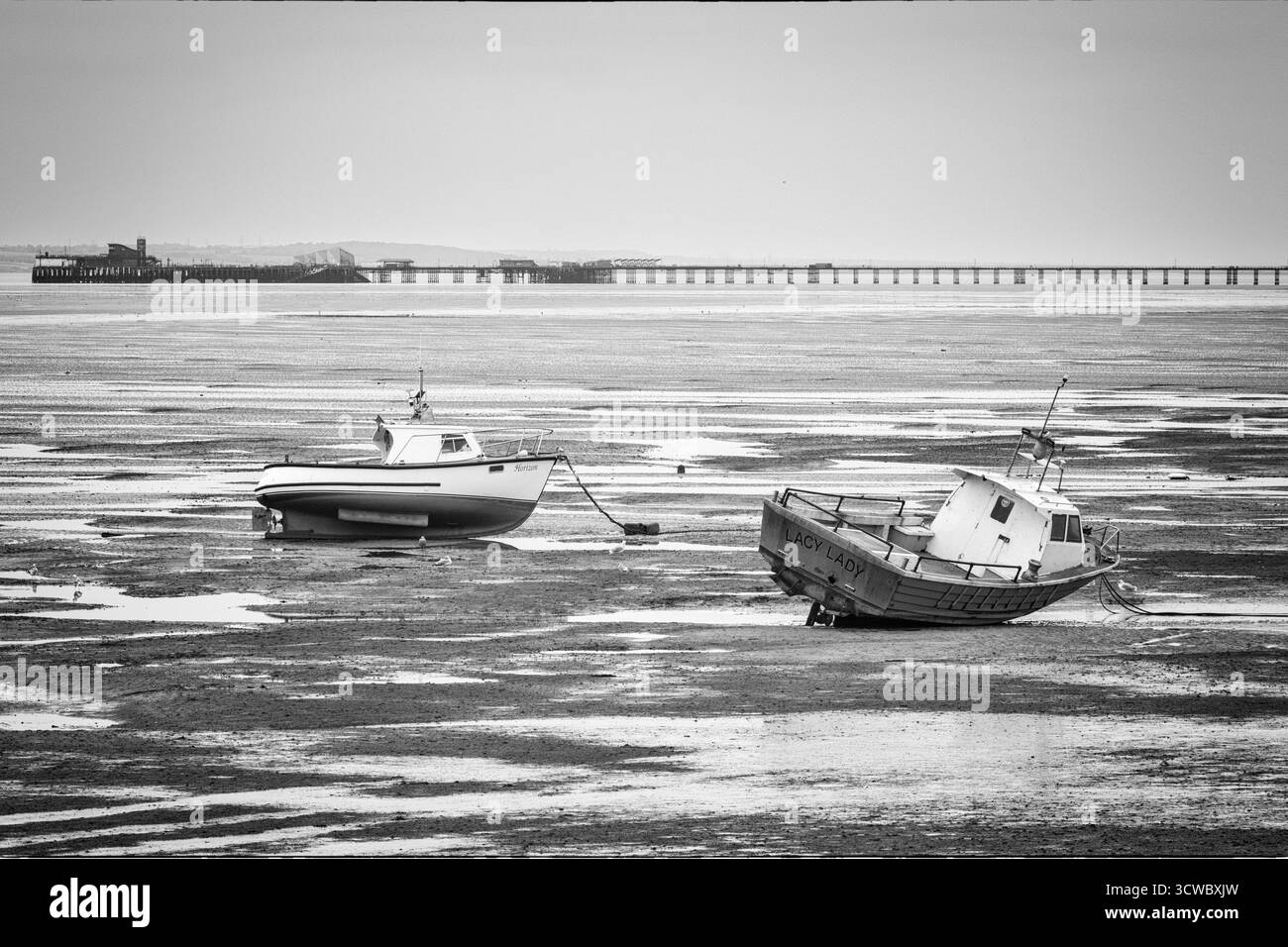 Barca a riposo sulle distese fangose al largo di Thorpe Bay in una mattinata di ottobre molto noiosa con il molo più lungo del mondo a Southend sullo sfondo Foto Stock
