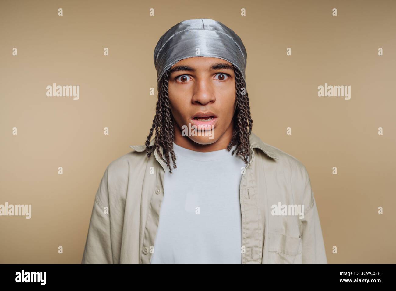 il ritratto di un giovane uomo dall'espressione sconvolta cattura un momento di vera sorpresa, mostrando il potere dell'emozione umana su sfondo beige Foto Stock