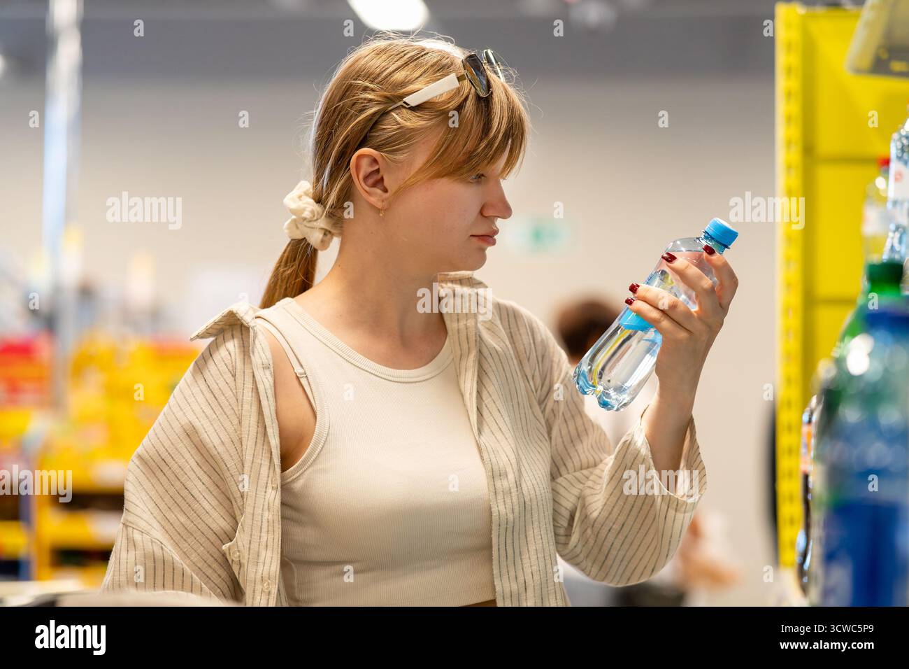 Consumo attento alla salute e verifica della qualità del prodotto. Donna che legge attentamente l'etichetta degli ingredienti sulla bottiglia d'acqua durante lo shopping al supermercato. Foto Stock