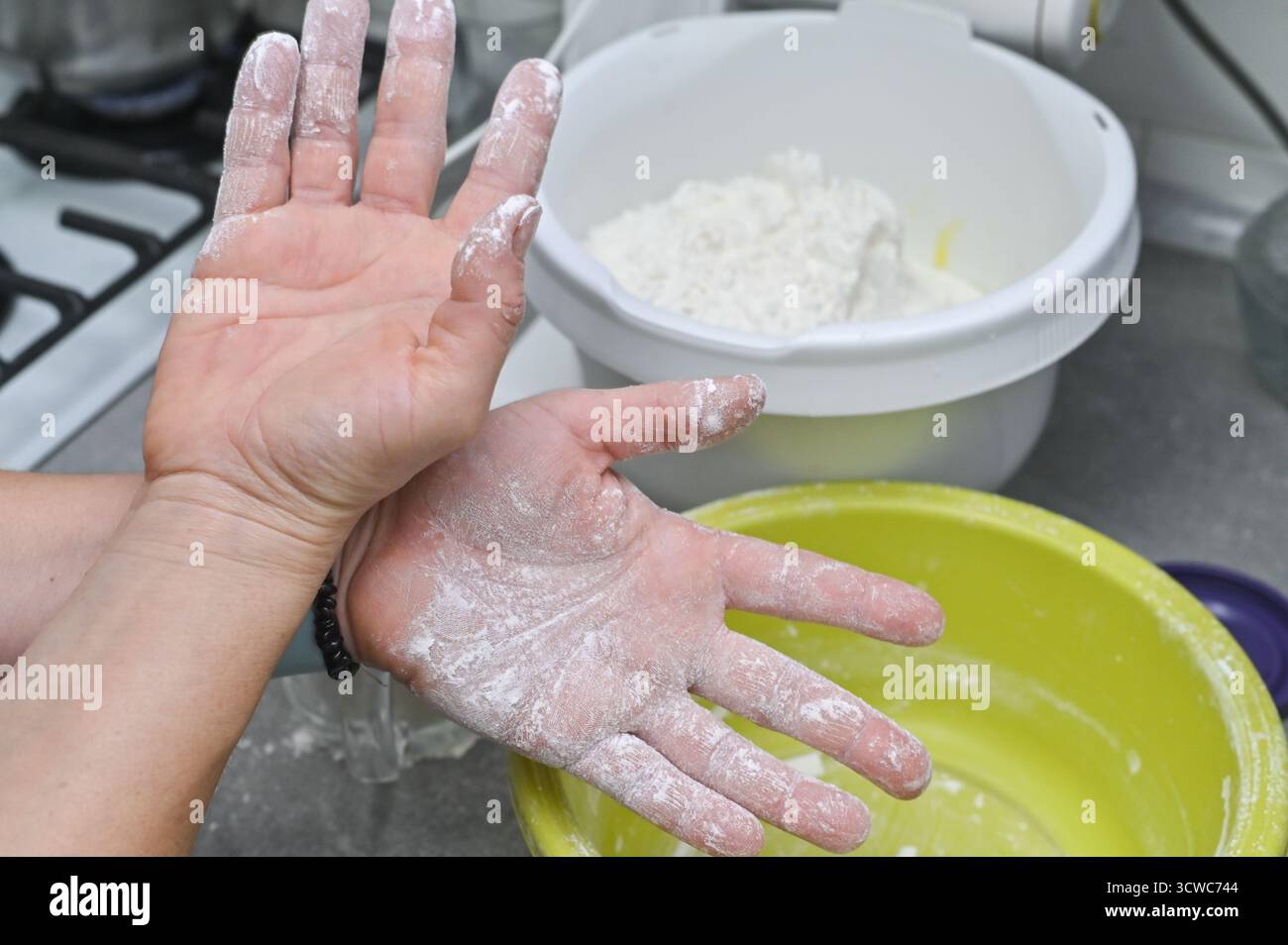 Ricoperto a mano di farina durante il processo di cottura. Cottura casalinga che rappresenta la preparazione dell'impasto e la tradizione culinaria. Primo piano delle mani con la farina in ki Foto Stock