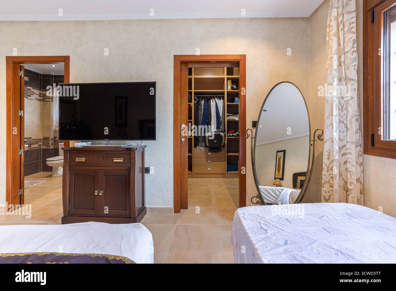 Gli interni contemporanei della camera da letto presentano una grande TV a schermo piatto su un piedistallo in legno, una cabina armadio visibile con deposito vestiti organizzato e un completo Foto Stock