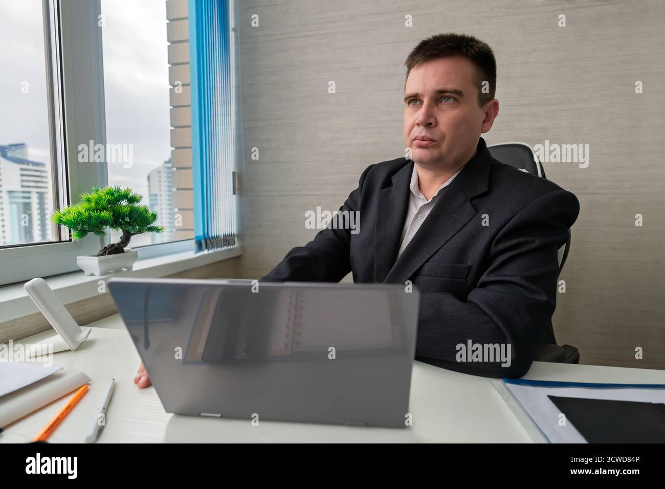 Uomo professionista che lavora su un notebook a una scrivania moderna durante il giorno in un elegante spazio di lavoro. Un uomo d'affari viene distratto dalle conversazioni Foto Stock