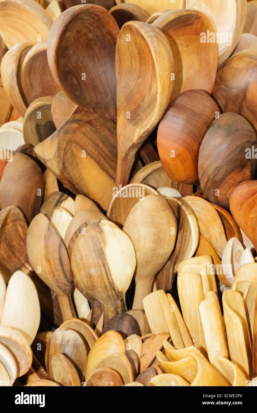 Primo piano di una collezione di cucchiai di legno fatti a mano in varie tonalità e grani di legno. L'immagine mette in evidenza l'abilità artigianale, i materiali organici e. Foto Stock