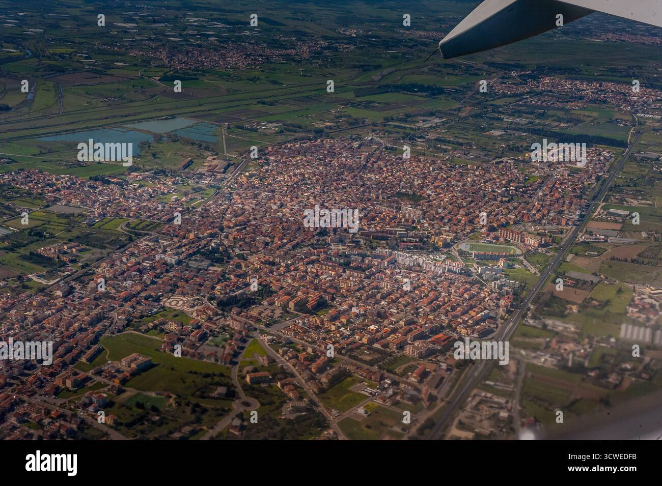 Veduta aerea di Assemini, vicino a Cagliari, Sardegna, con paesaggio urbano, prati verdi, e la struttura della città dalla finestra dell'aereo Foto Stock