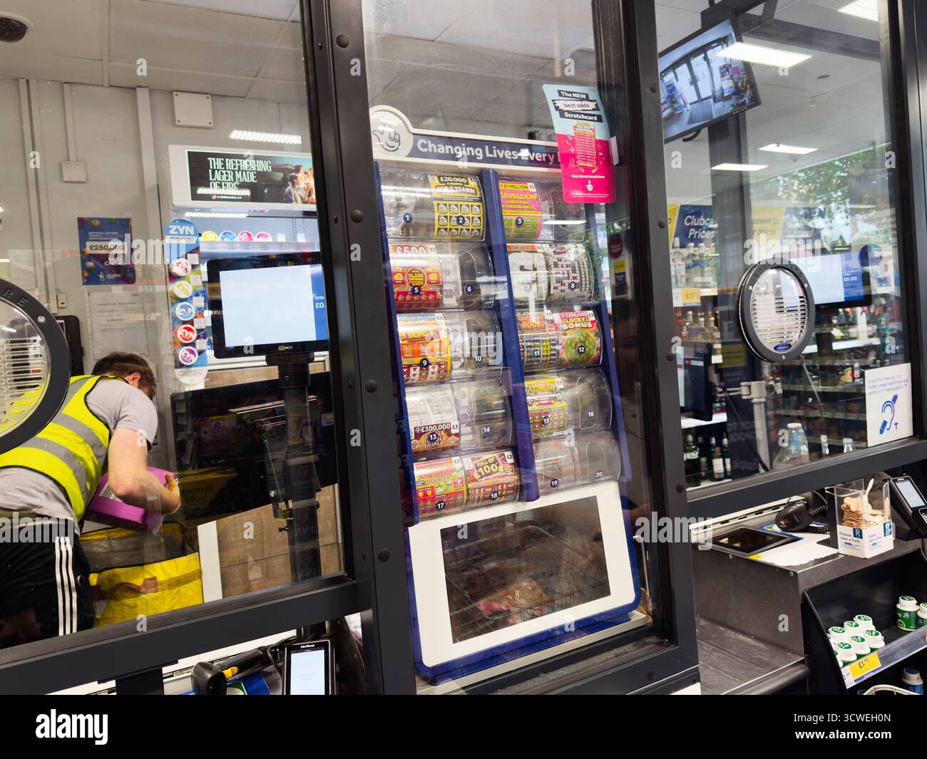 Manchester, Regno Unito - 26 settembre 2025: Interno del negozio di scommesse affollato con slot machine, cassa e un membro del personale in un giubbotto. Foto Stock