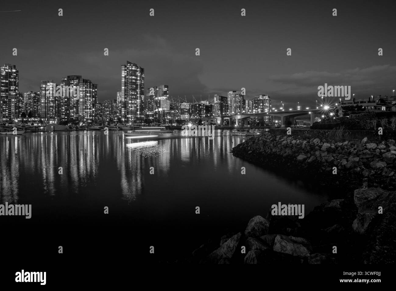 I luminosi edifici della città illuminano la riva, creando riflessi nell'acqua calma durante la notte in una città costiera. Foto Stock