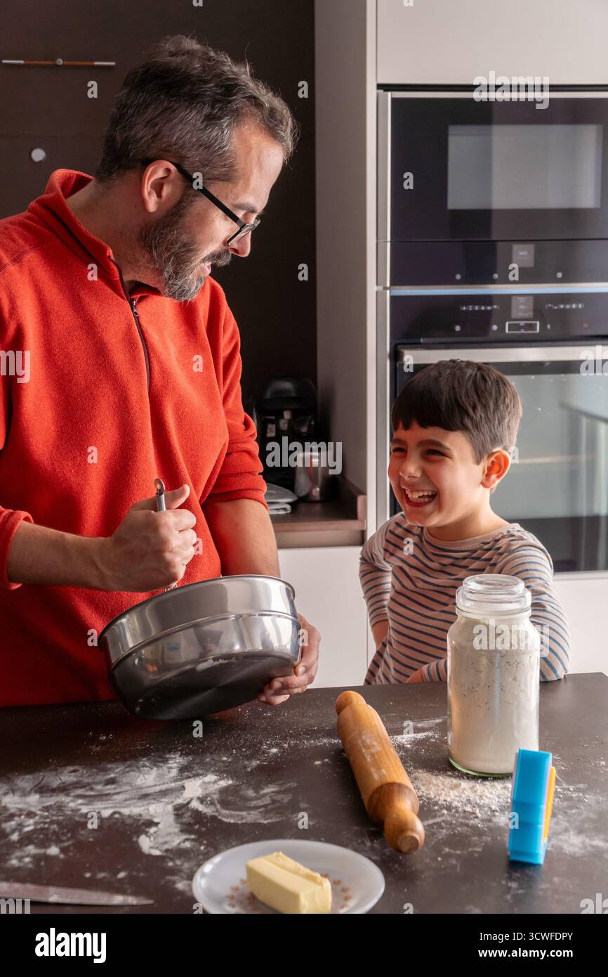 Padre e figlio di generazione alfa che cucinano biscotti di natale in una cucina disordinata Foto Stock