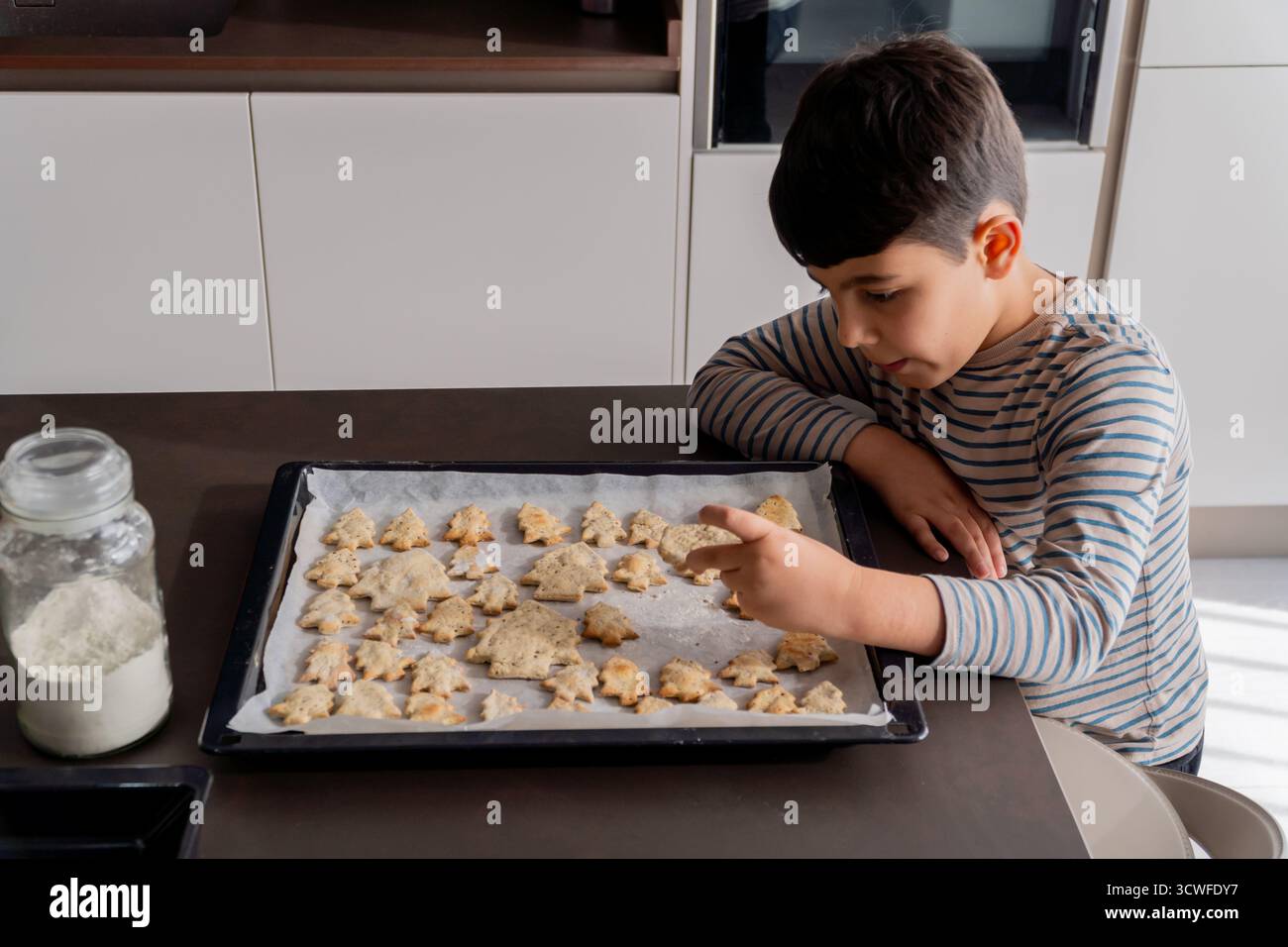 Generazione alfa che raccoglie un biscotto fatto in casa con la forma dell'albero di natale Foto Stock