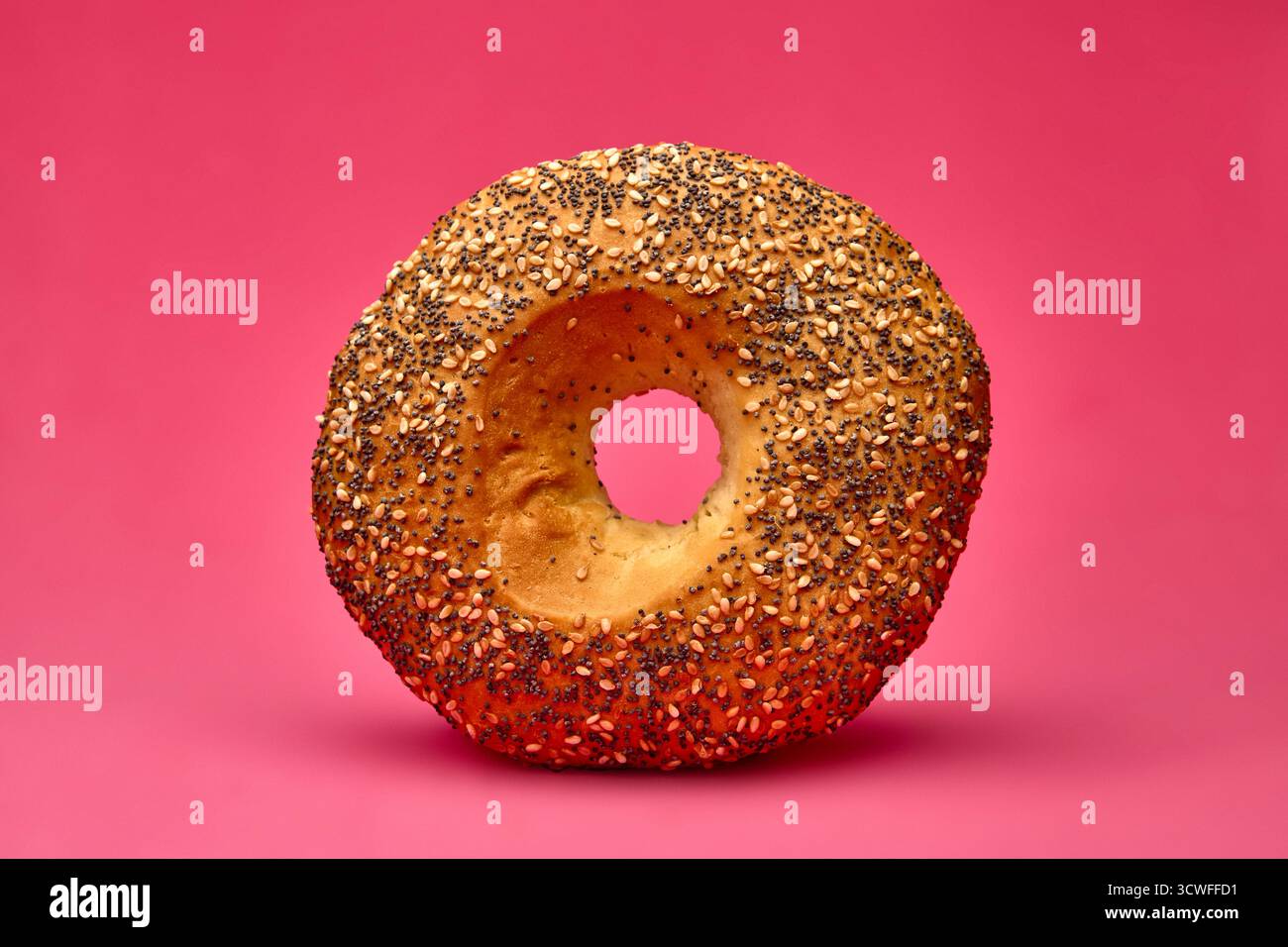 Primo piano di un singolo panino rotondo cosparso di semi di papavero, isolato su un vivace sfondo rosa. Immagine perfetta per la pubblicità di prodotti da forno, breakfa Foto Stock